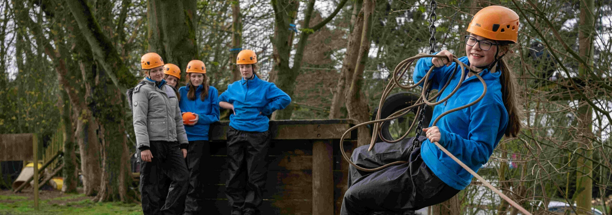 A young person wearing an orange helmet and blue coat standing in a tyre on an obstacle course.