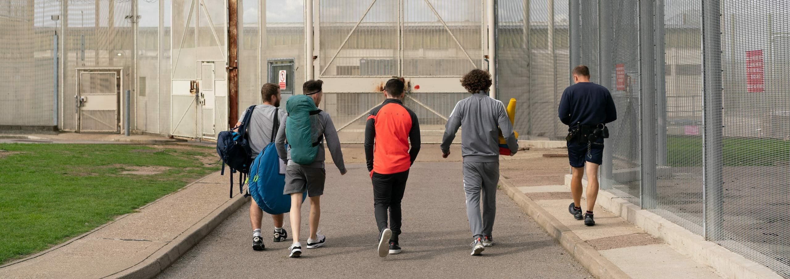 Four young offenders and a prison officer walking towards tall gates.