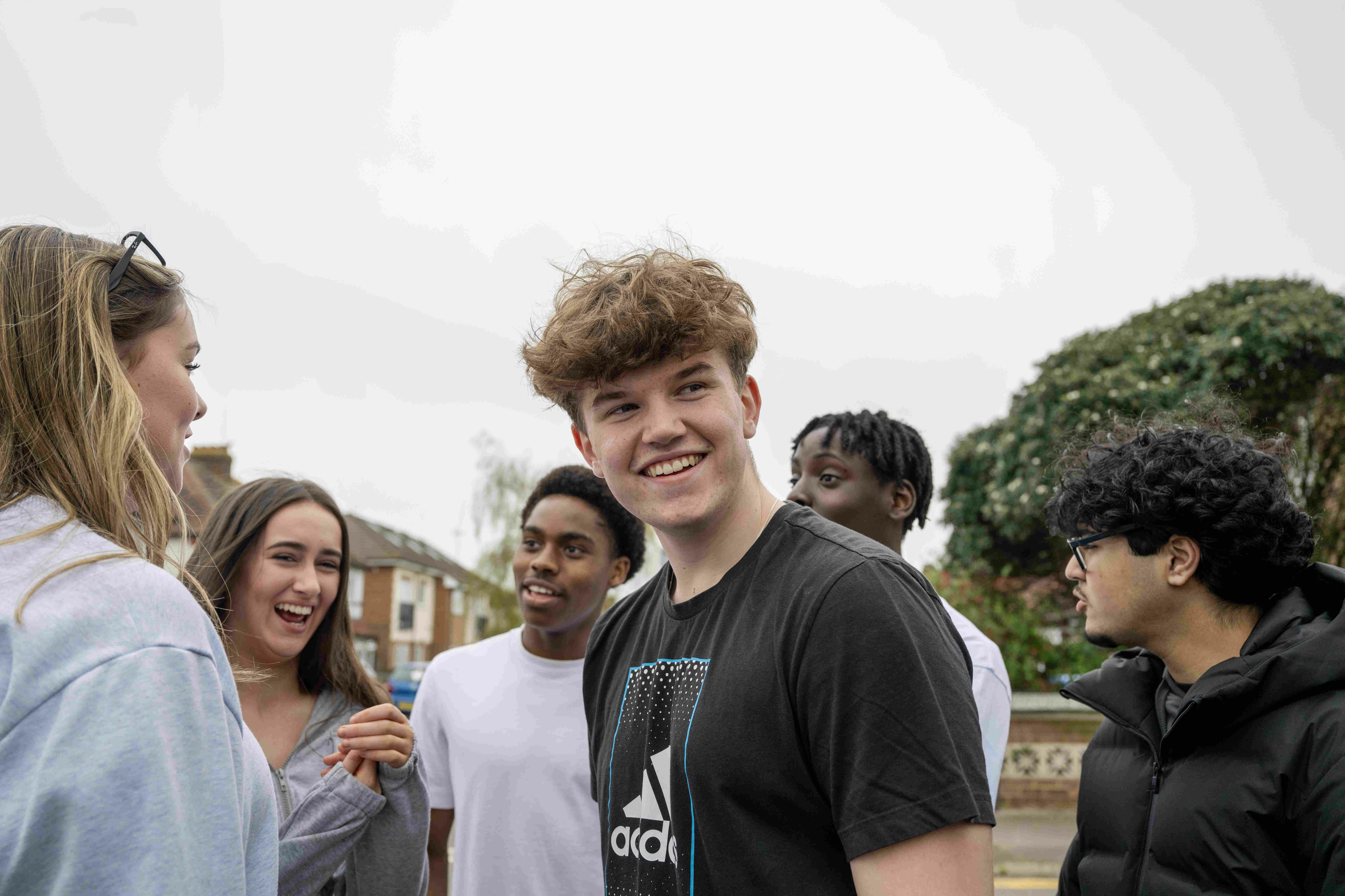 A crowd of young people, a man is in focus, surrounded by two women and three men.