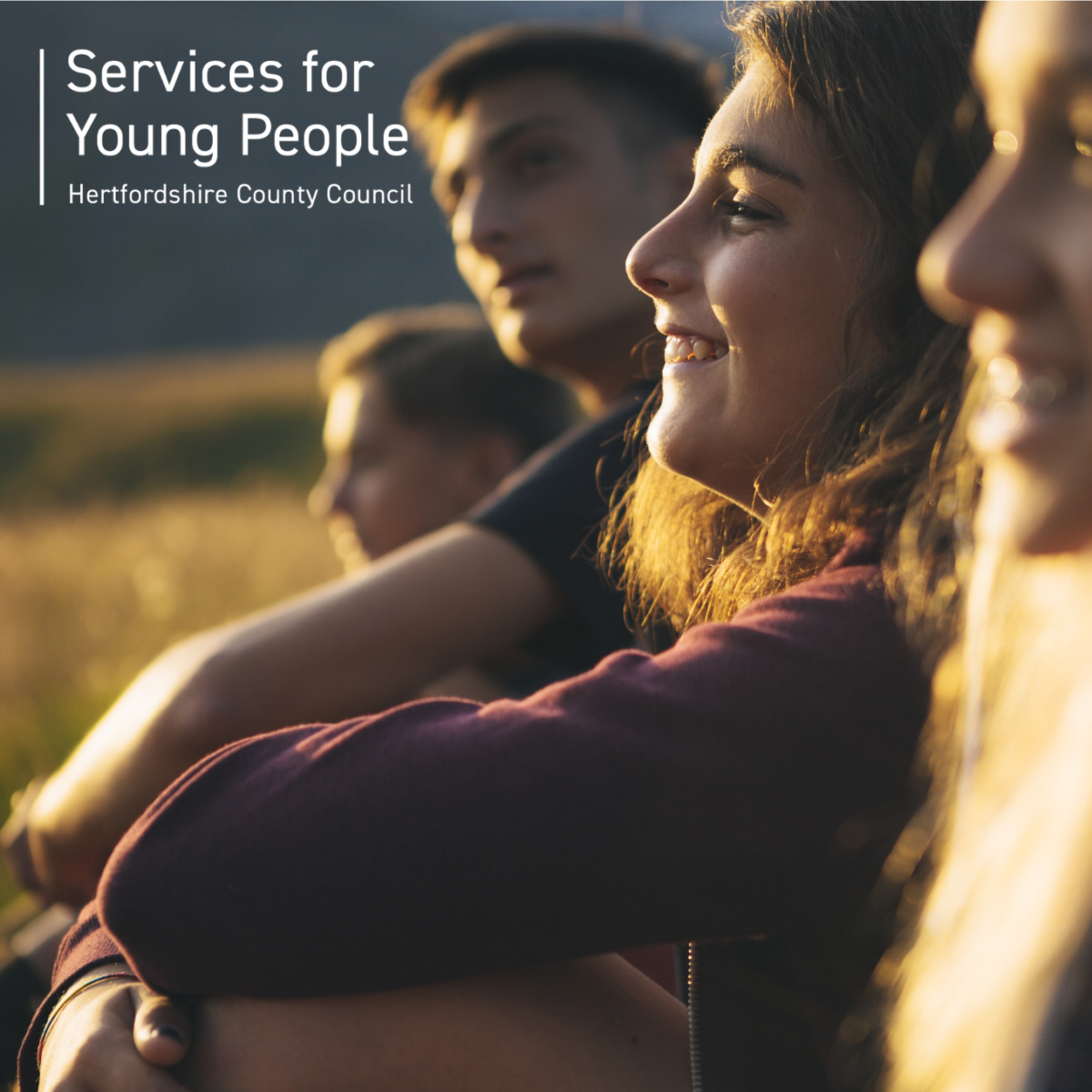 Close-up of a small group of young people outdoors in warm, golden sunlight, sitting together and looking into the distance. Overlaid text on the left reads “Services for Young People” and “Hertfordshire County Council.