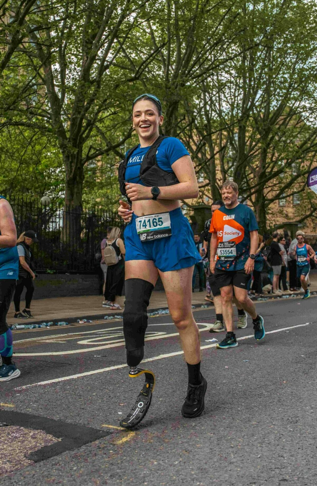 Milly smiling while running a race, she has a blue t-shirt and shorts, and a black prosthetic leg.