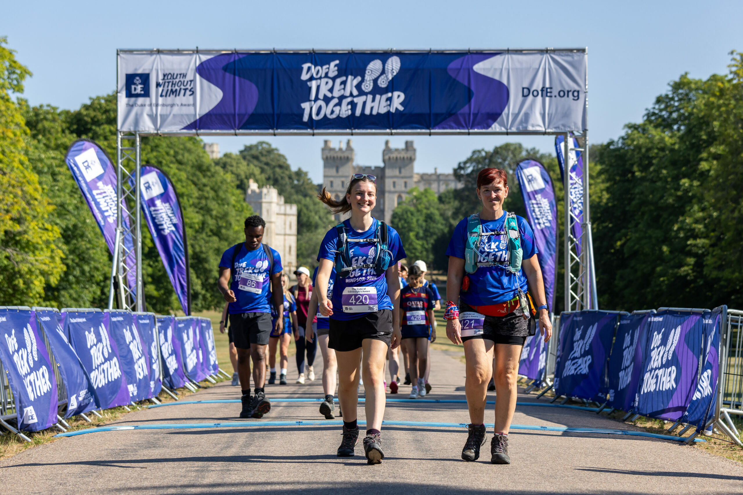 Participants cross the Trek Together finish line on a sunny day, with Windsor Castle in the background.