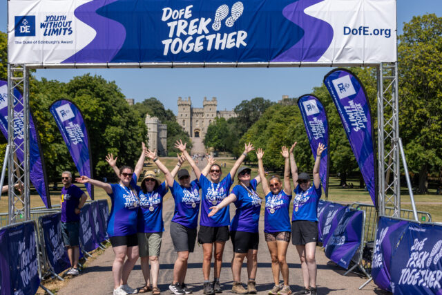 A group of Trek Together participants pose beneath the finish arch, with Windsor Castle in the background.