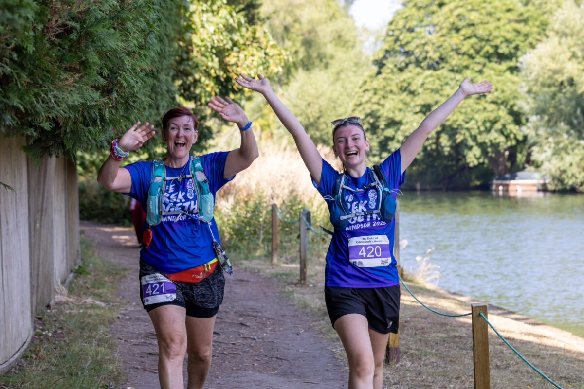 Two Trek Together participants walk along a riverside path with their arms raised during the event.