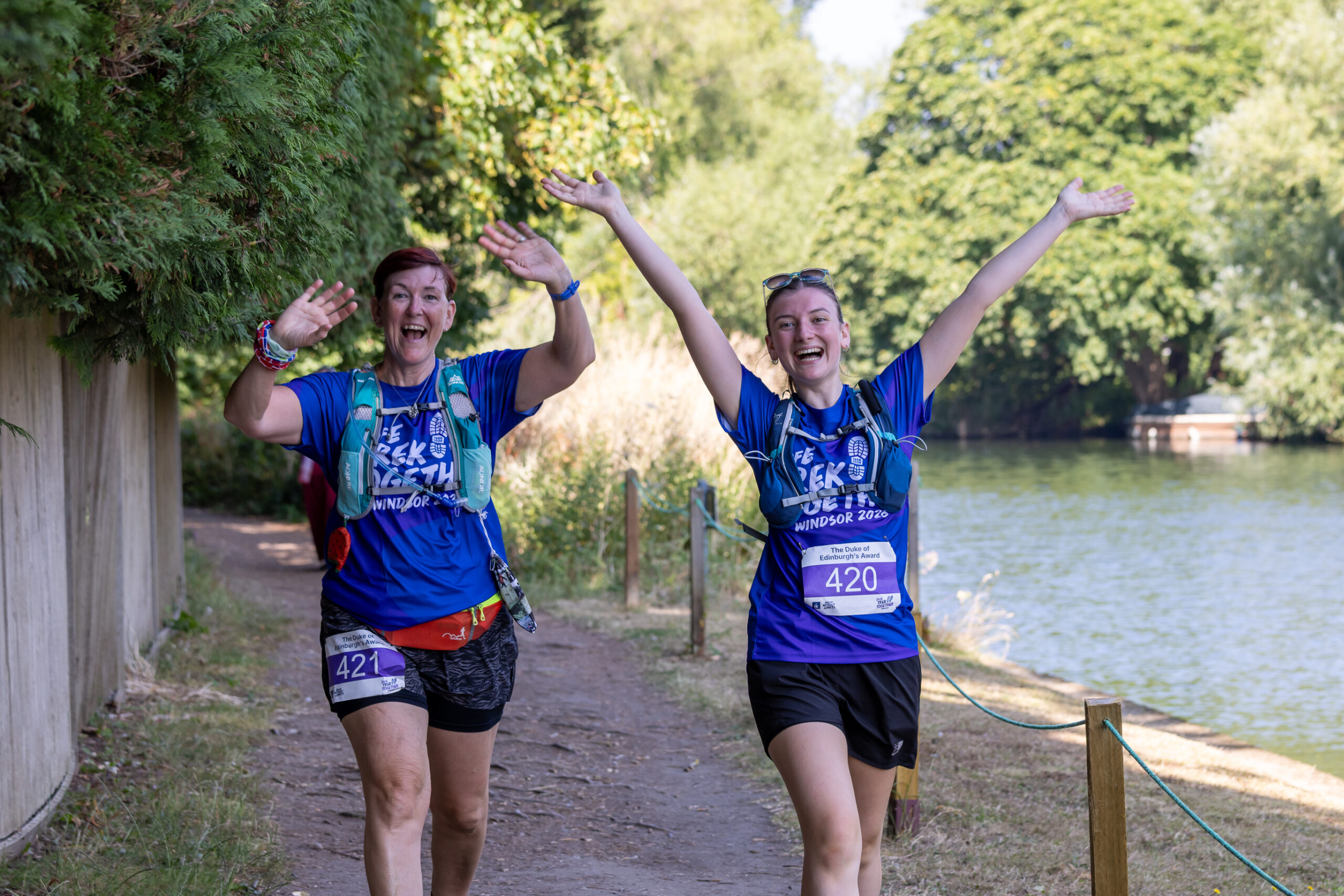 Two Trek Together participants walk along a riverside path with their arms raised during the event.