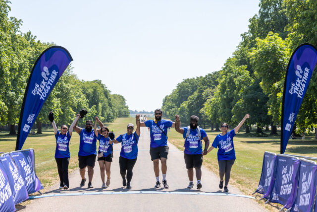 A group of Trek Together participants cross the finish line together with raised arms.