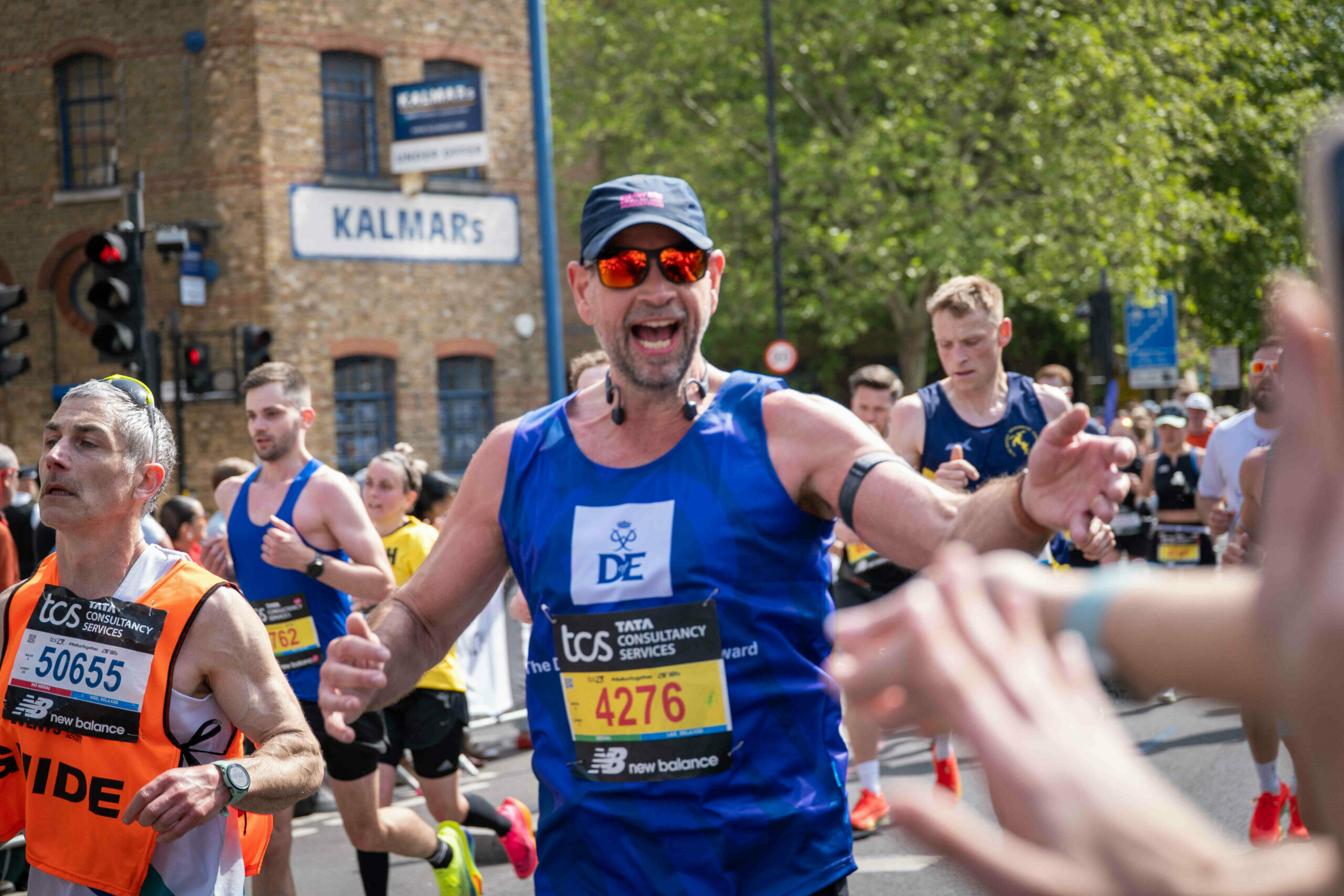 A runner in the London Marathon reaching out and smiling, he's wearing a blue D of E running top.