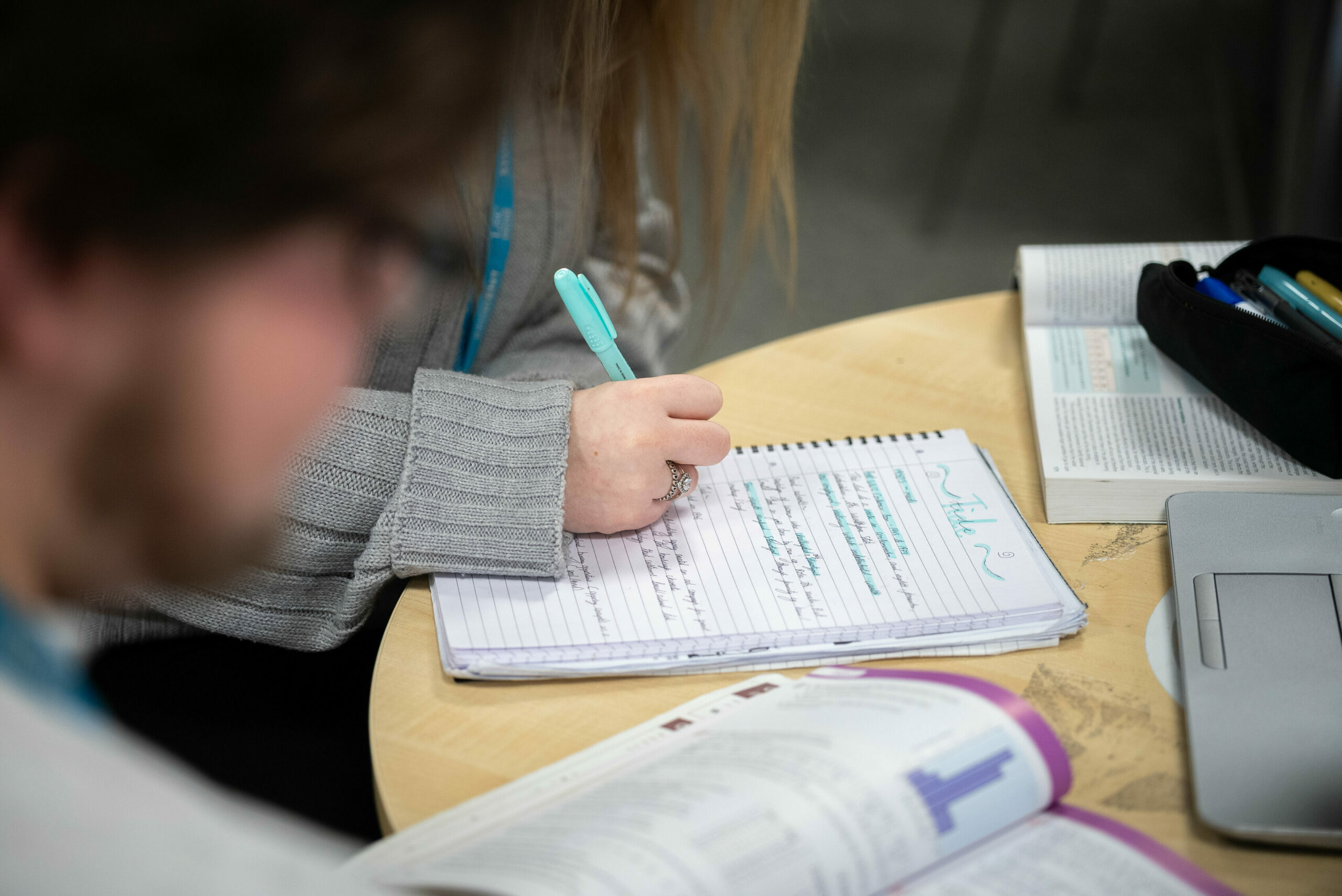 A person's hand writing in a notebook with a turquoise pen.