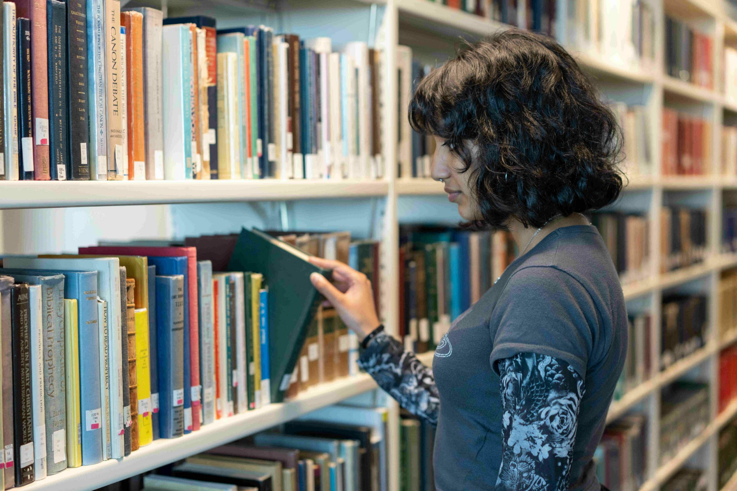 A young person picking a book out of a shelf in a library.