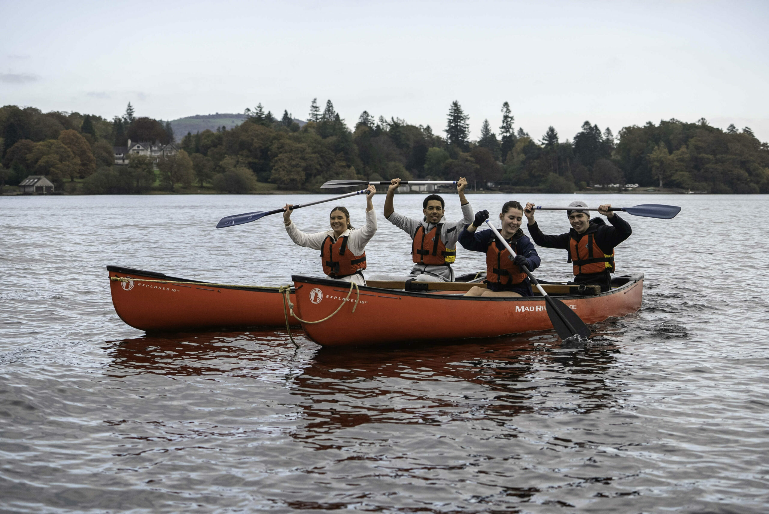 Four young people in two red canoes holding up their oars and smiling.