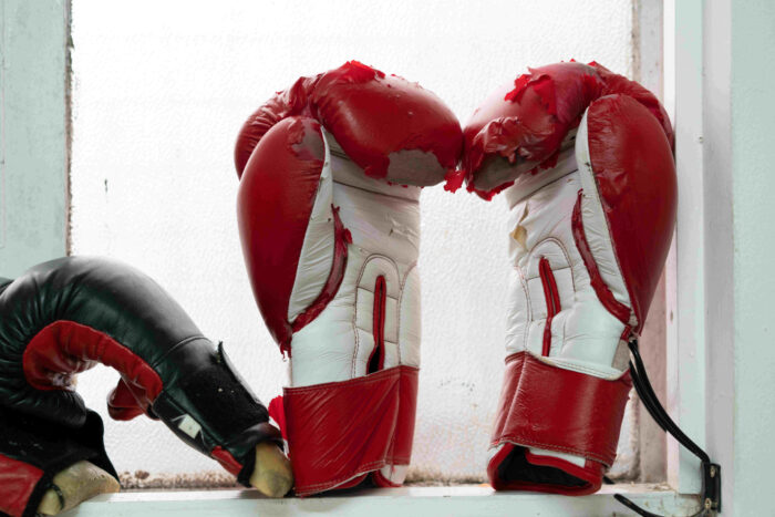 A pair of worn red and white boxing gloves resting against a white wall.