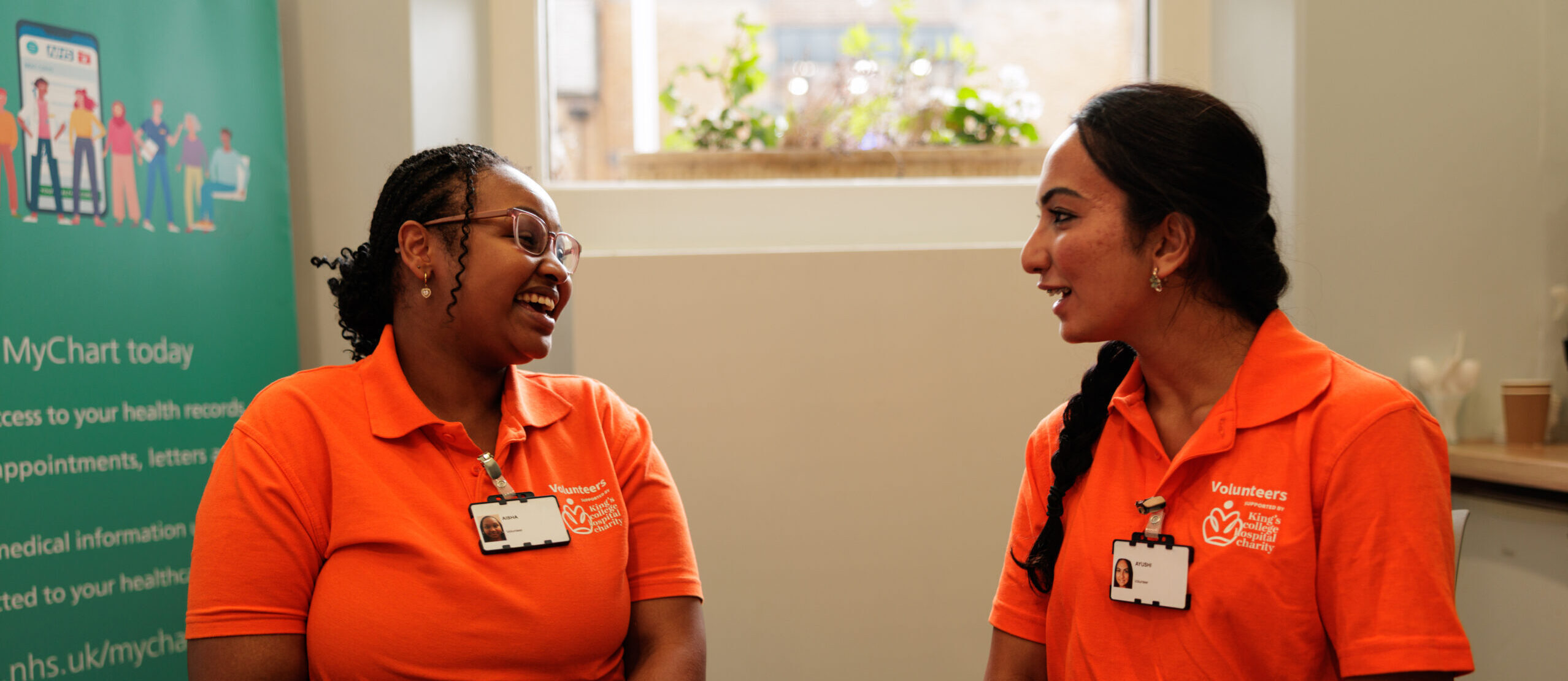 Two volunteers in orange polo shirts sit and talk across a table.