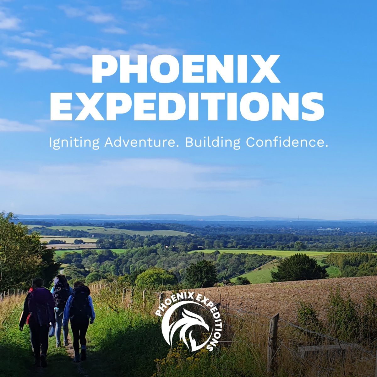 Phoenix Expeditions promotional image showing a group of hikers walking along a countryside path through rolling green hills under a bright blue sky. Large white text reads “PHOENIX EXPEDITIONS” with the tagline “Igniting Adventure. Building Confidence.” A Phoenix Expeditions logo is displayed at the bottom of the image.
