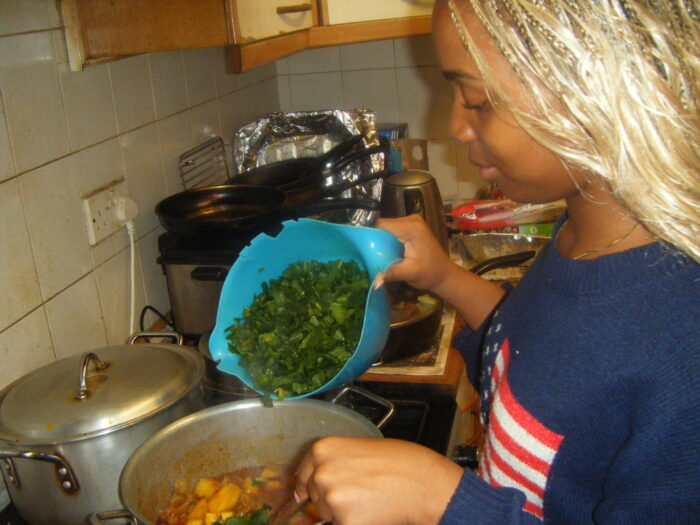 Faith chopped greens to a pot while cooking a meal in a kitchen.
