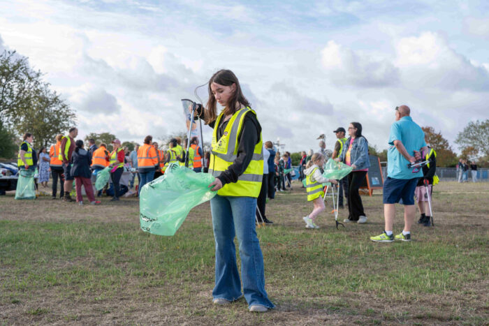 Person in a high-visibility vest holding a litter picker and recycling bag during a community litter pick.