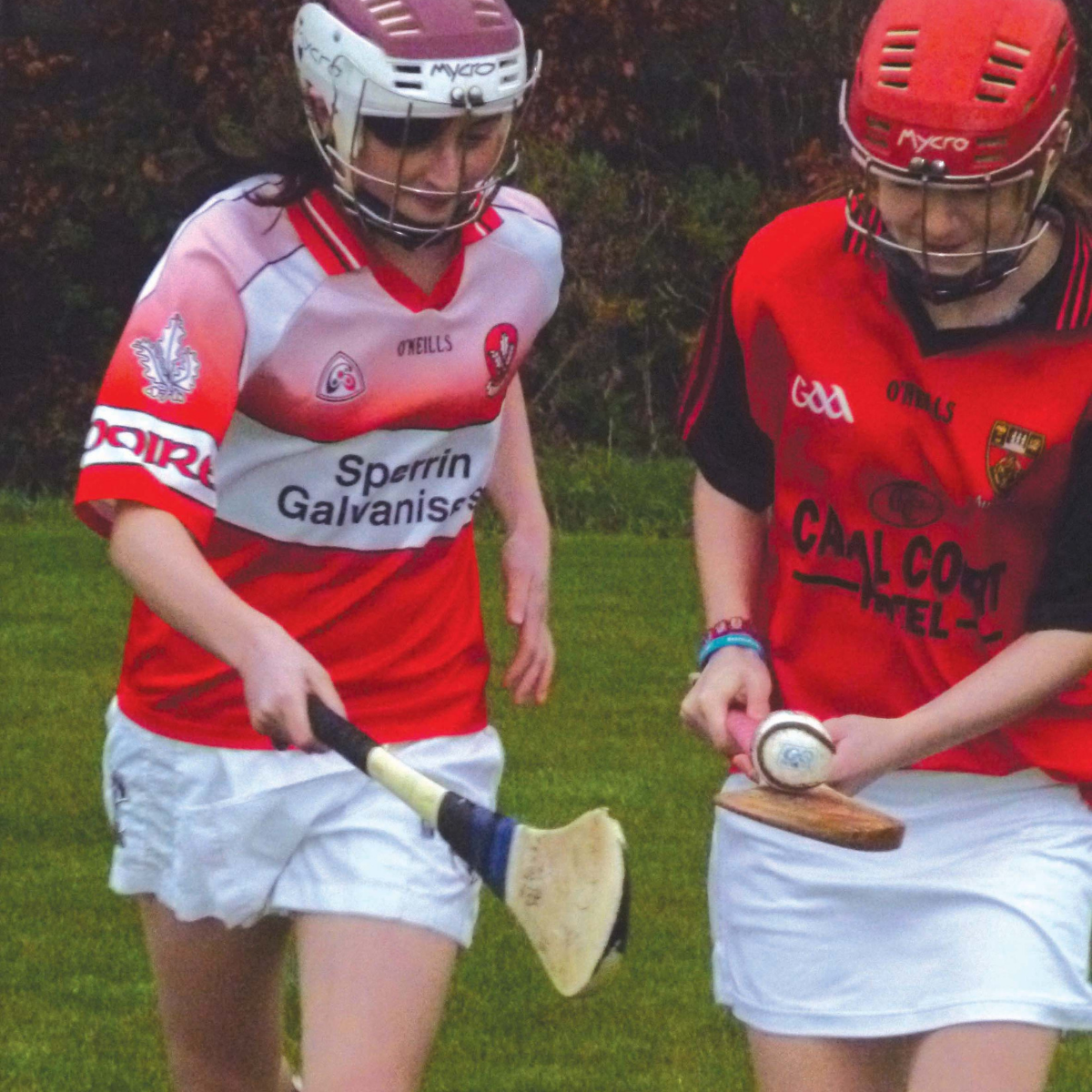 Two girls playing sports wearing helmets in red sports kit