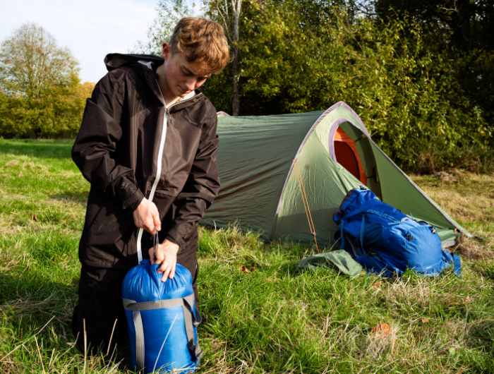 Young man packing sleeping bag in front of tent