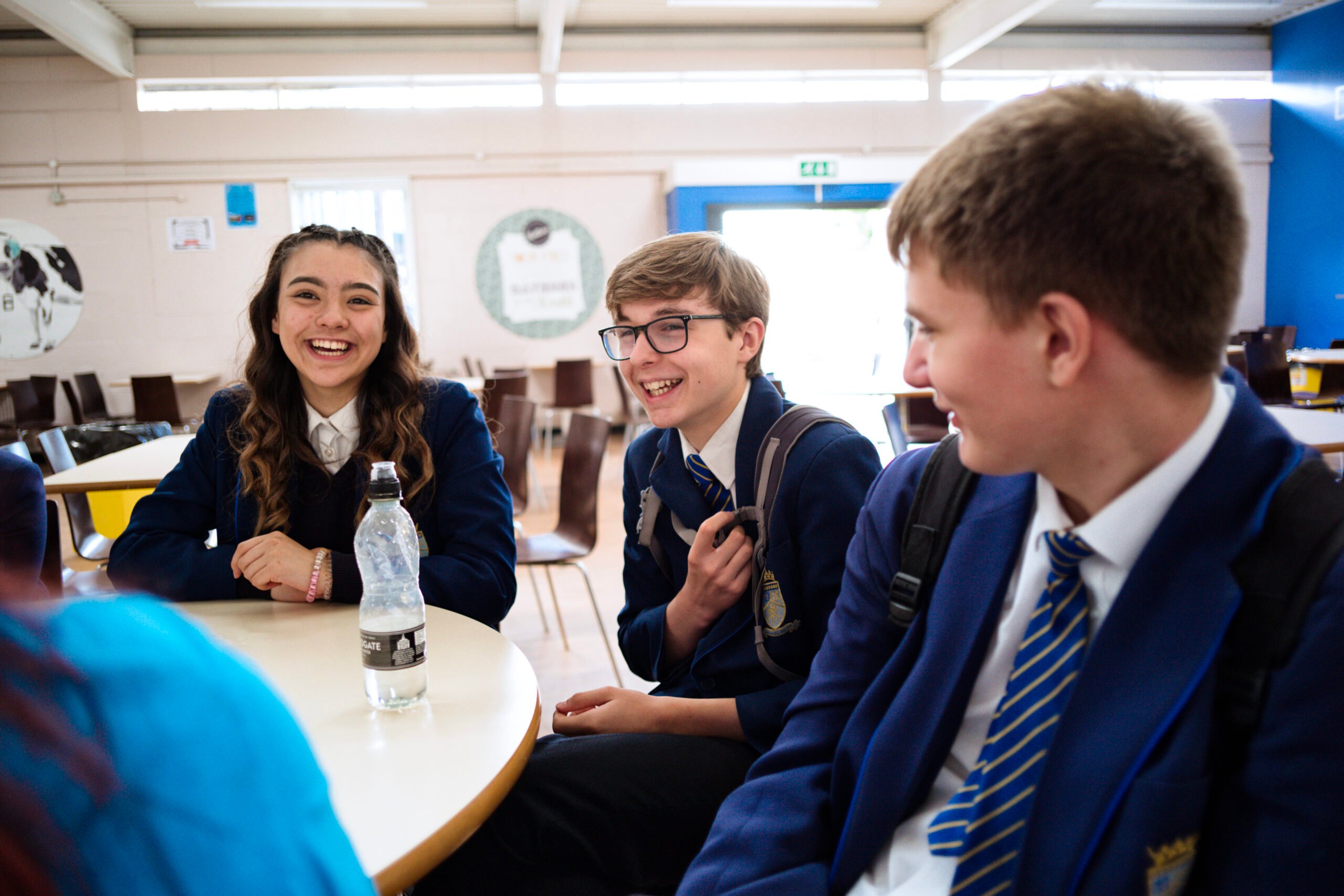 One girl and two boys wearing school uniform sat around a table laughing and smiling