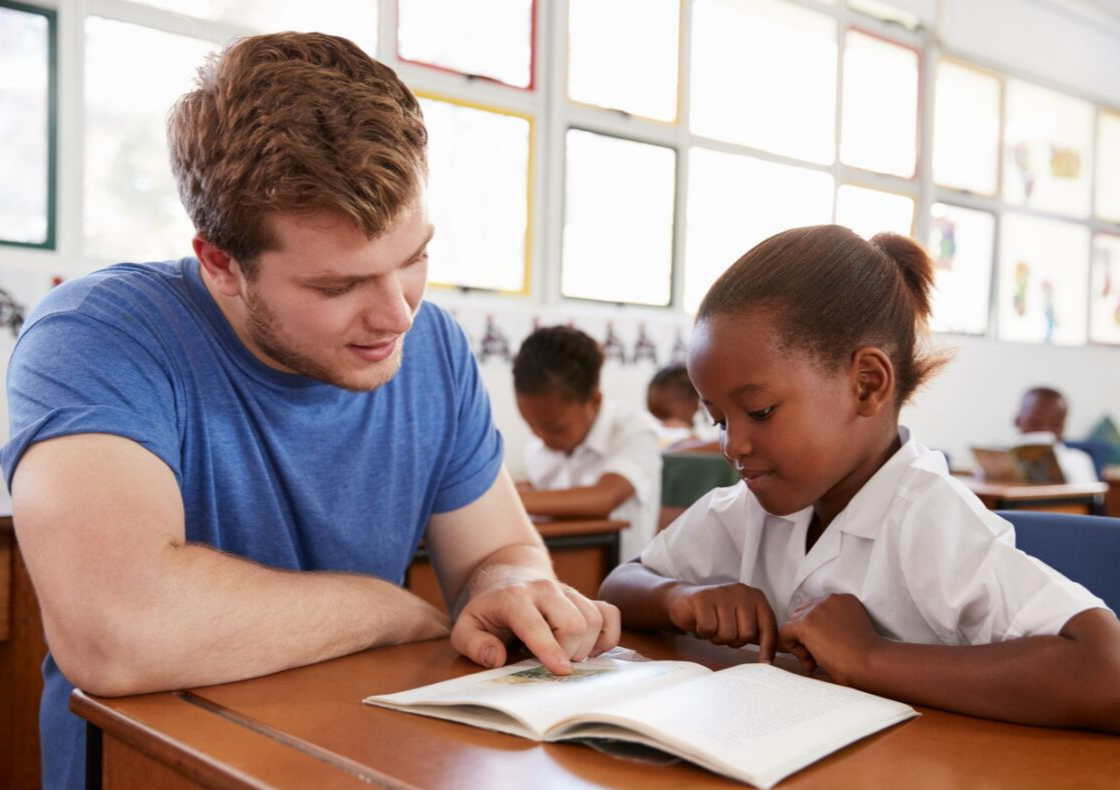 Young male teaching female child to read in classroom