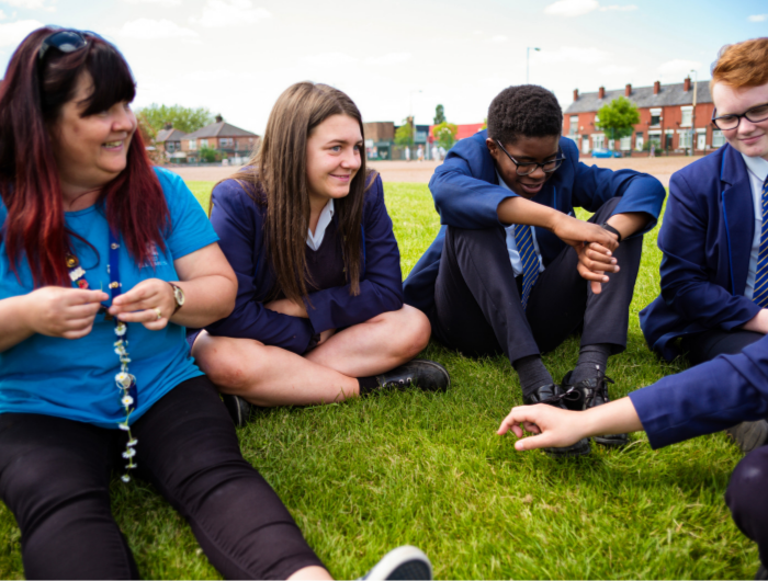 Leader and two participants in school uniforms outside making daisy chains