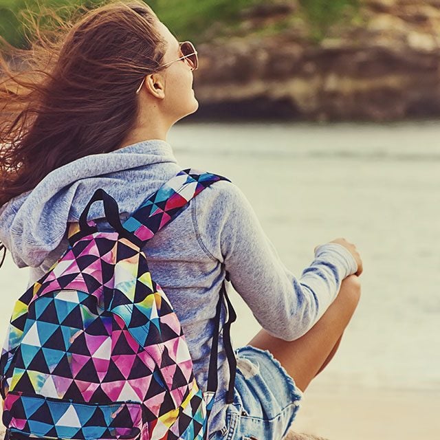 A young woman with backpack on a beach with wind in hair