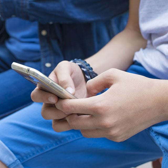 two young people sat together both on phone