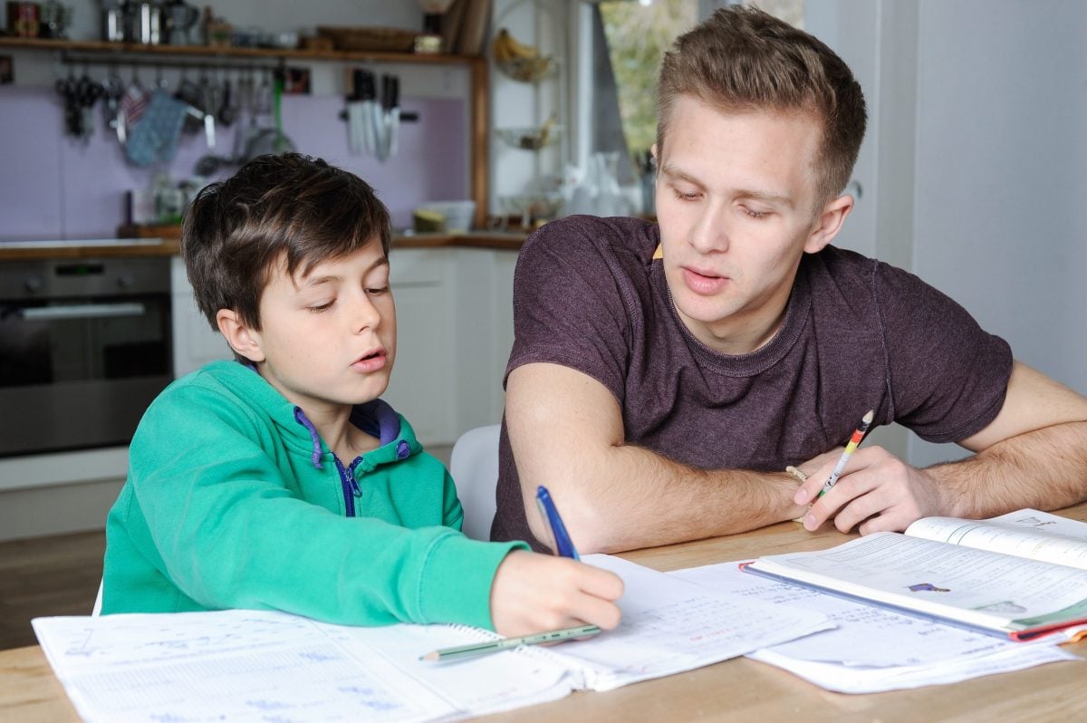 Young man helping younger male sibling with schoolwork