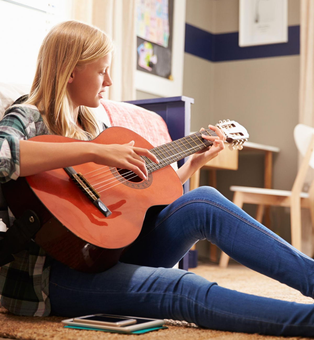Girl playing guitar sitting on bedroom floor
