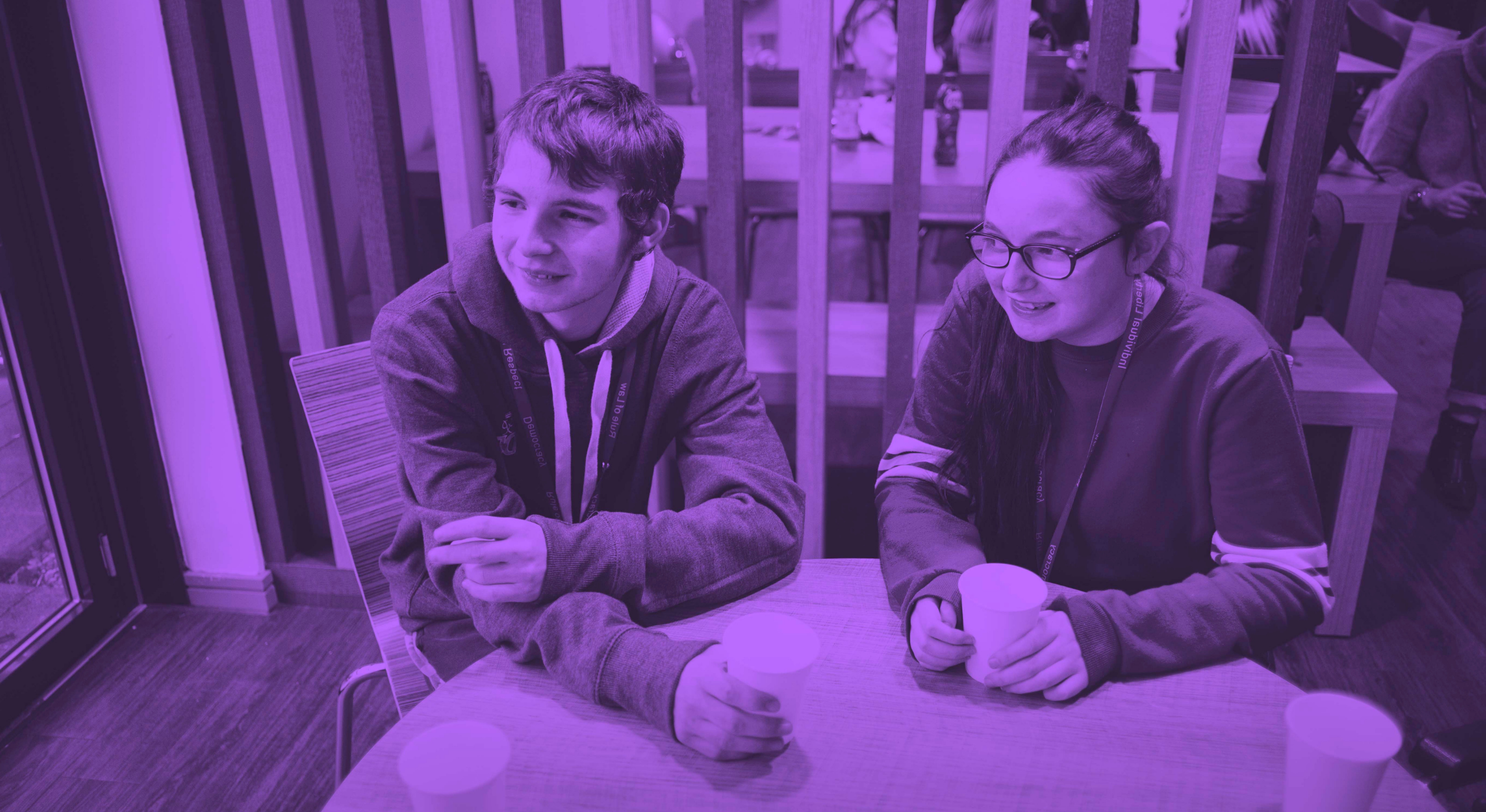 Young male and female students sitting at table holding coffee cups