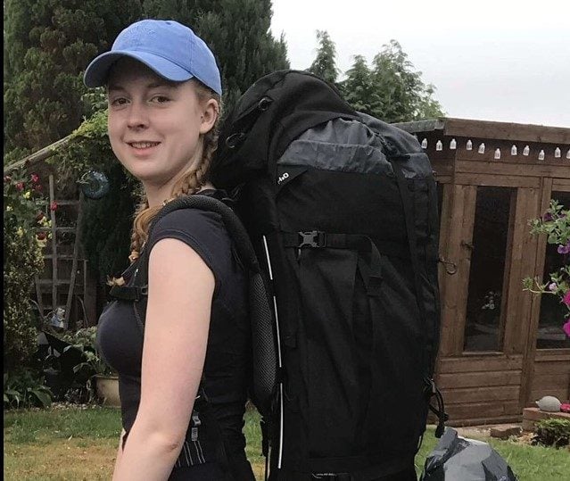 Lydia in black tshirt and blue cap wearing expedition backpack
