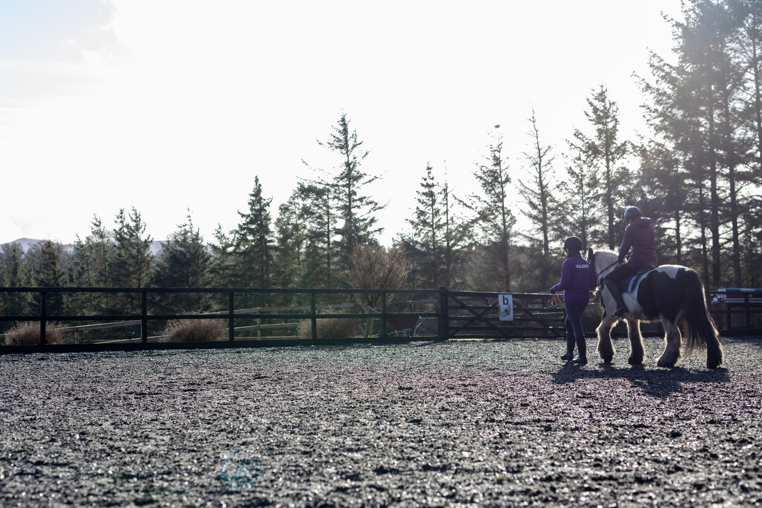 A young person riding a horse outside, with a person walking next to the horse holding the reins.