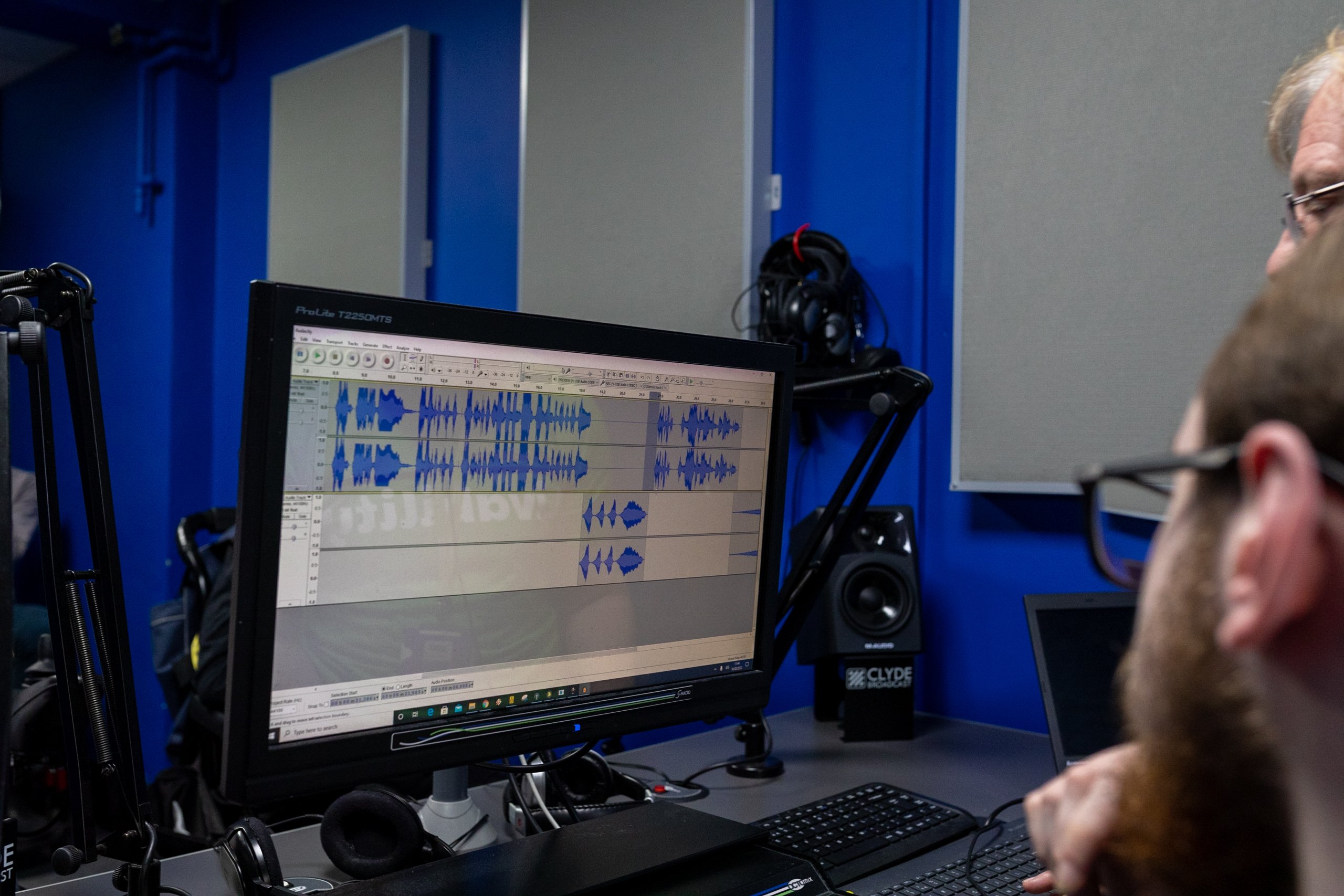 Two people looking at a computer screen displaying sound waves from a recording.