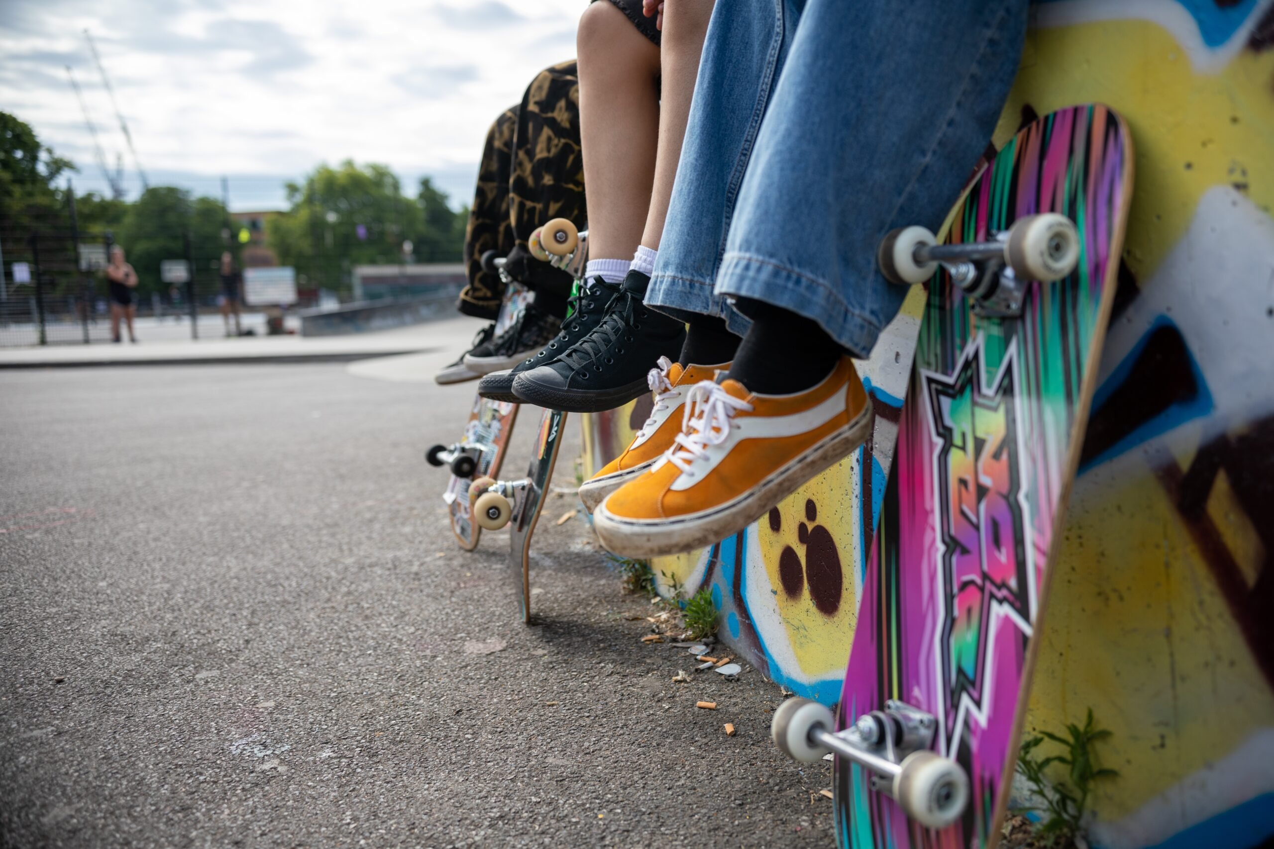 Three pairs of legs dangling off a ledge with colourful graffiti and skateboards leaning against it.