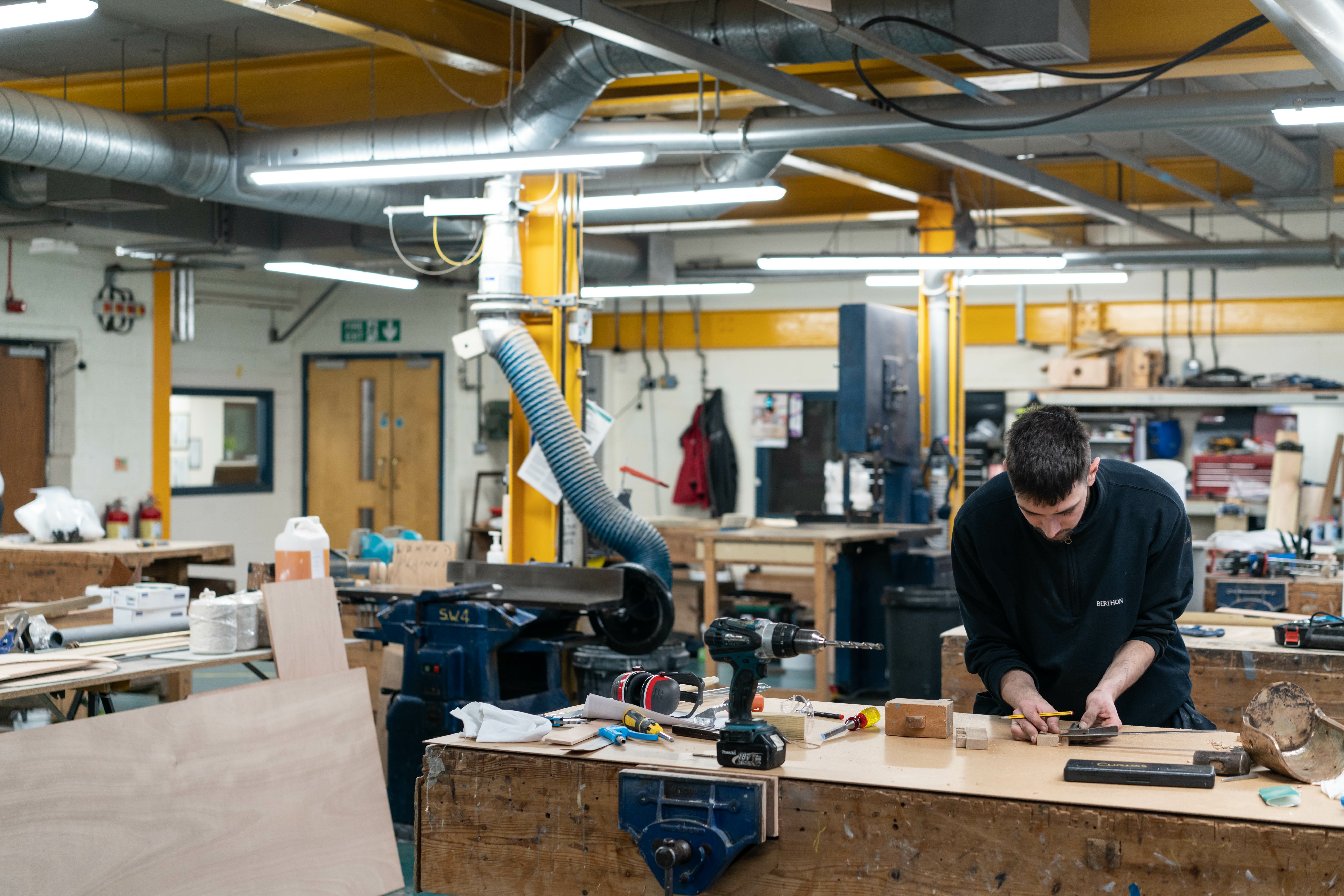 A young person leaning over a work bench in a boat yard workshop.