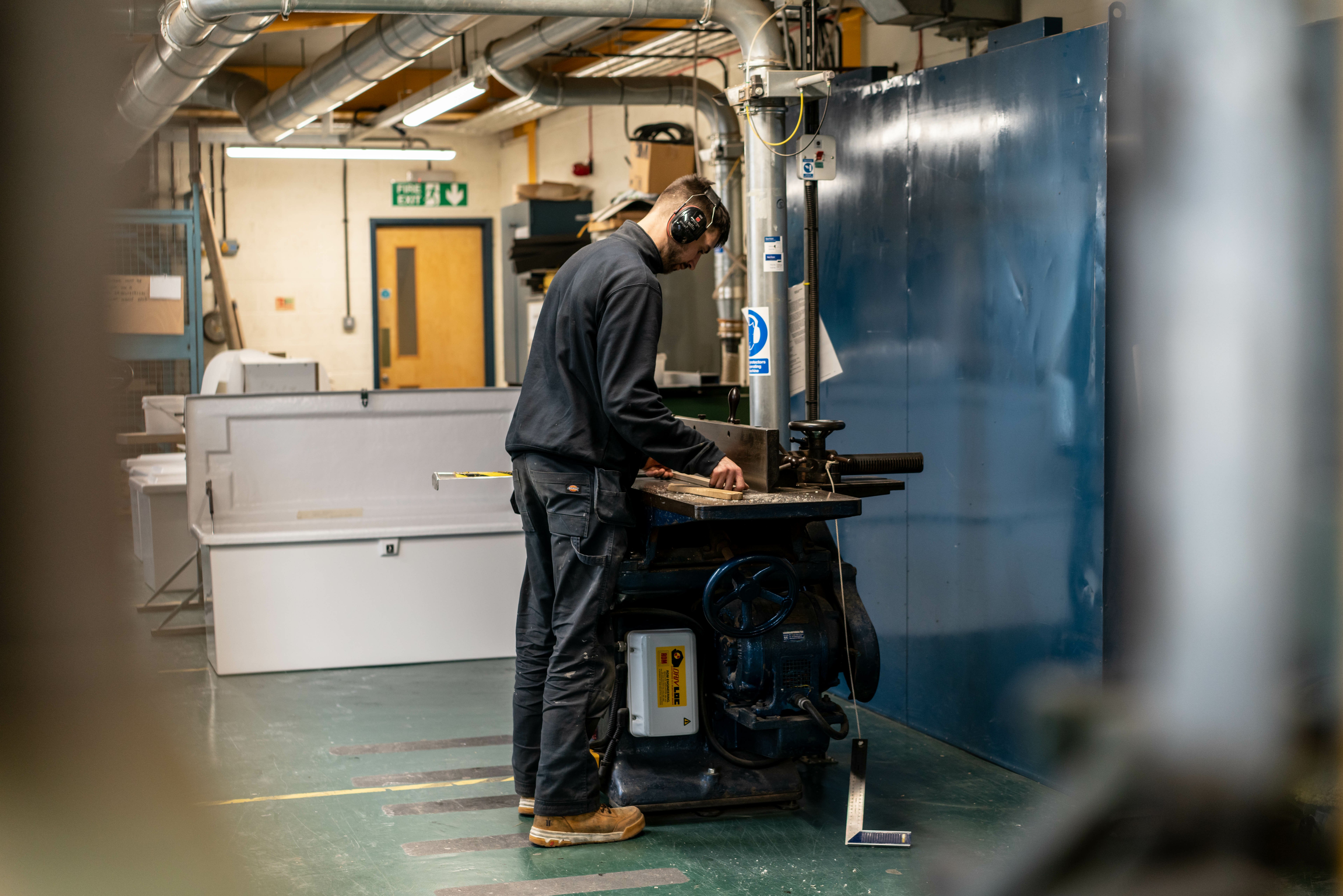 A young person planing a length of wood inside a workshop.