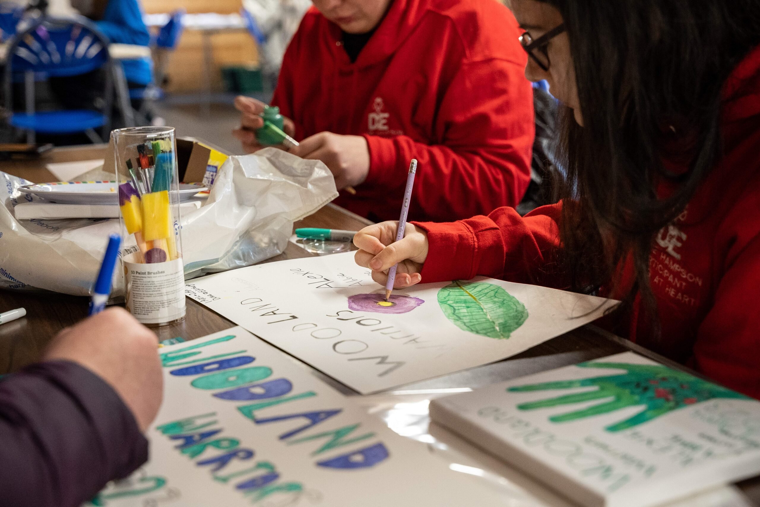 Young people sitting around a table painting signs that say woodland warriors.
