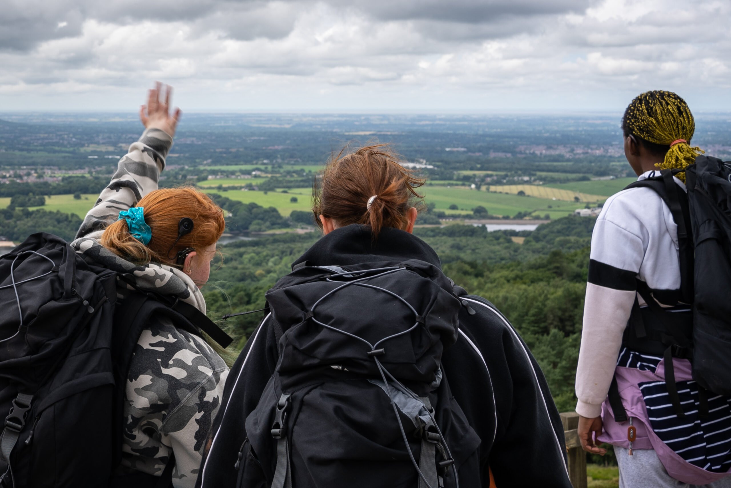 Three people looking at a view of green fields and forests.