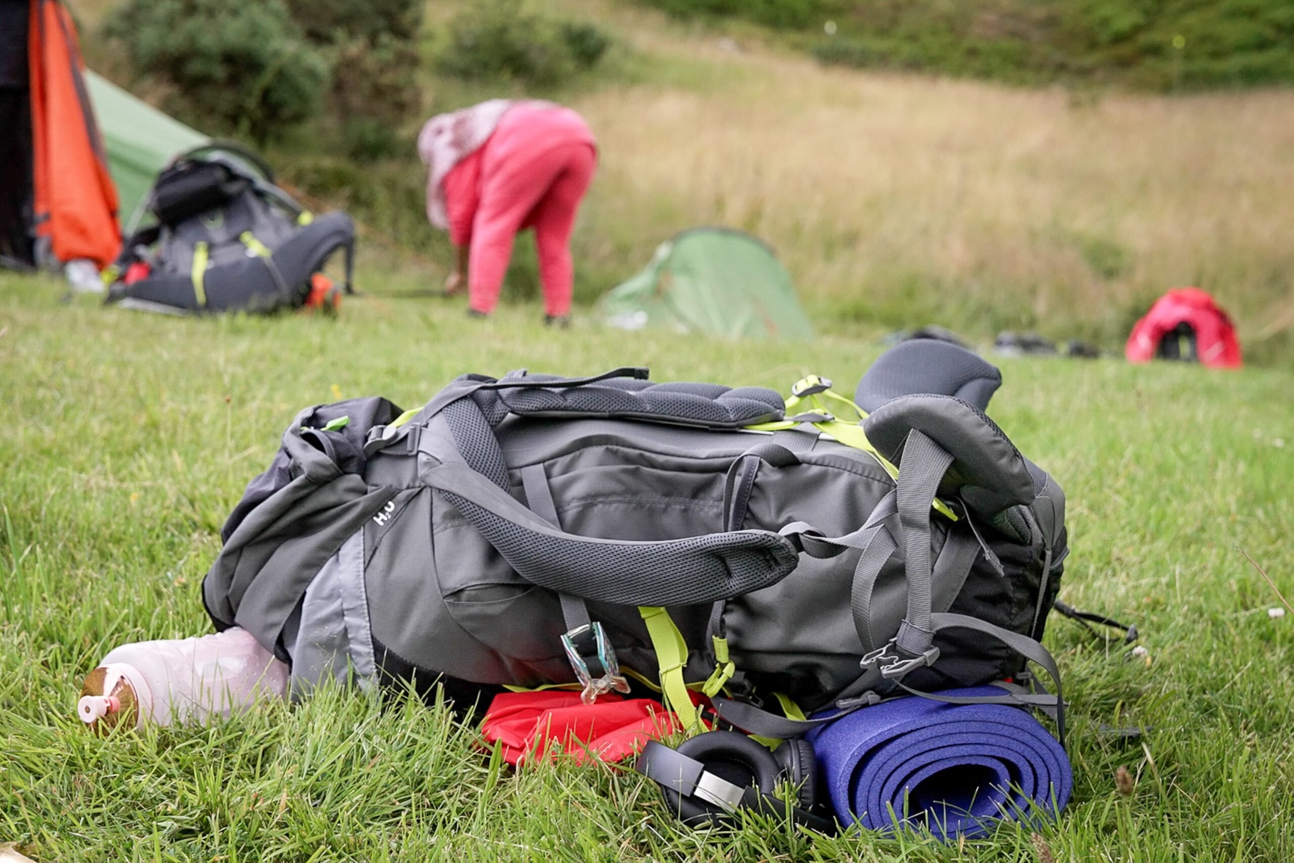 A rucksack with a water bottle, sleeping mat and headphones attached lying in the grass.