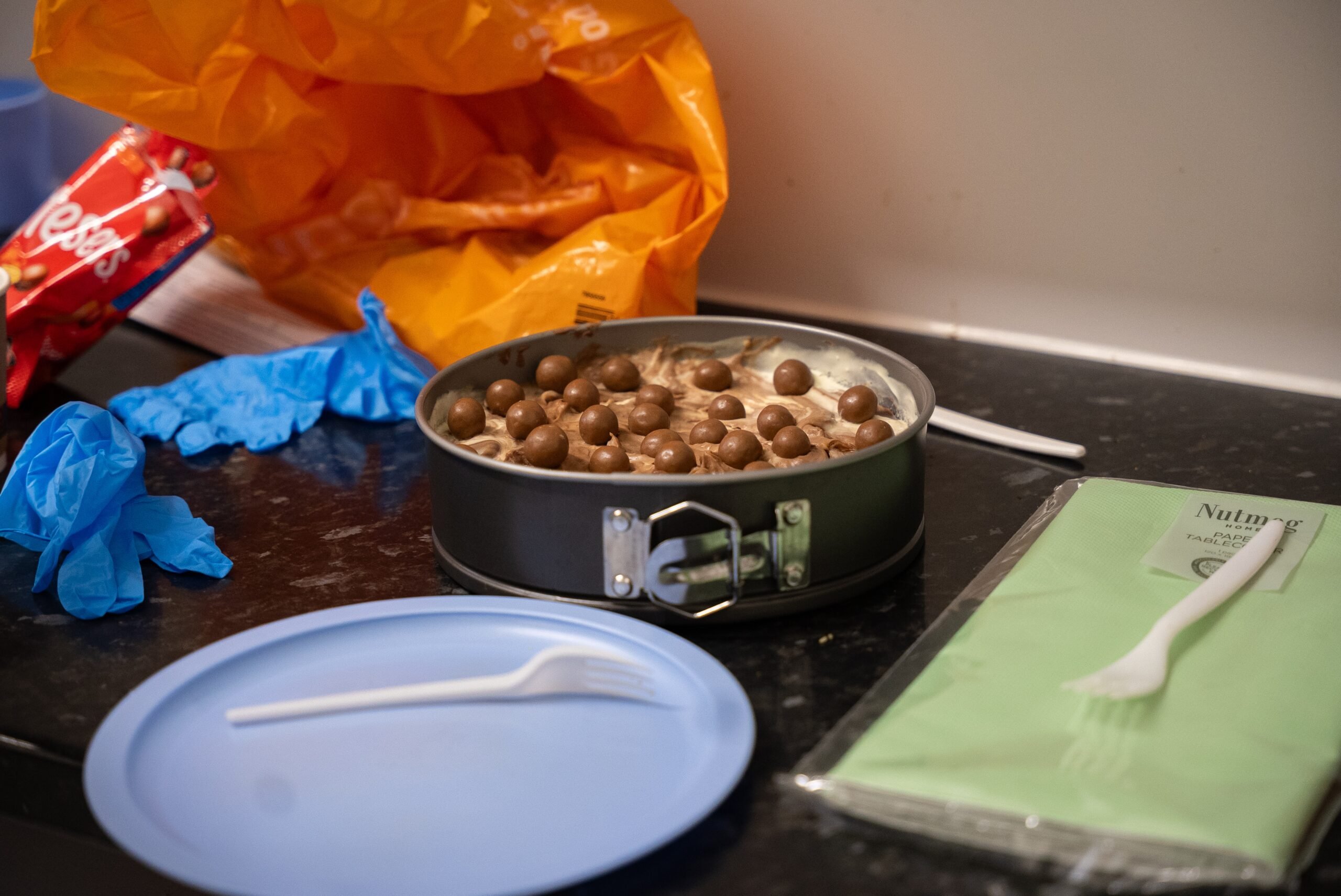 A cake topped with Maltesers sitting on a counter next to a plate, napkins and forks.