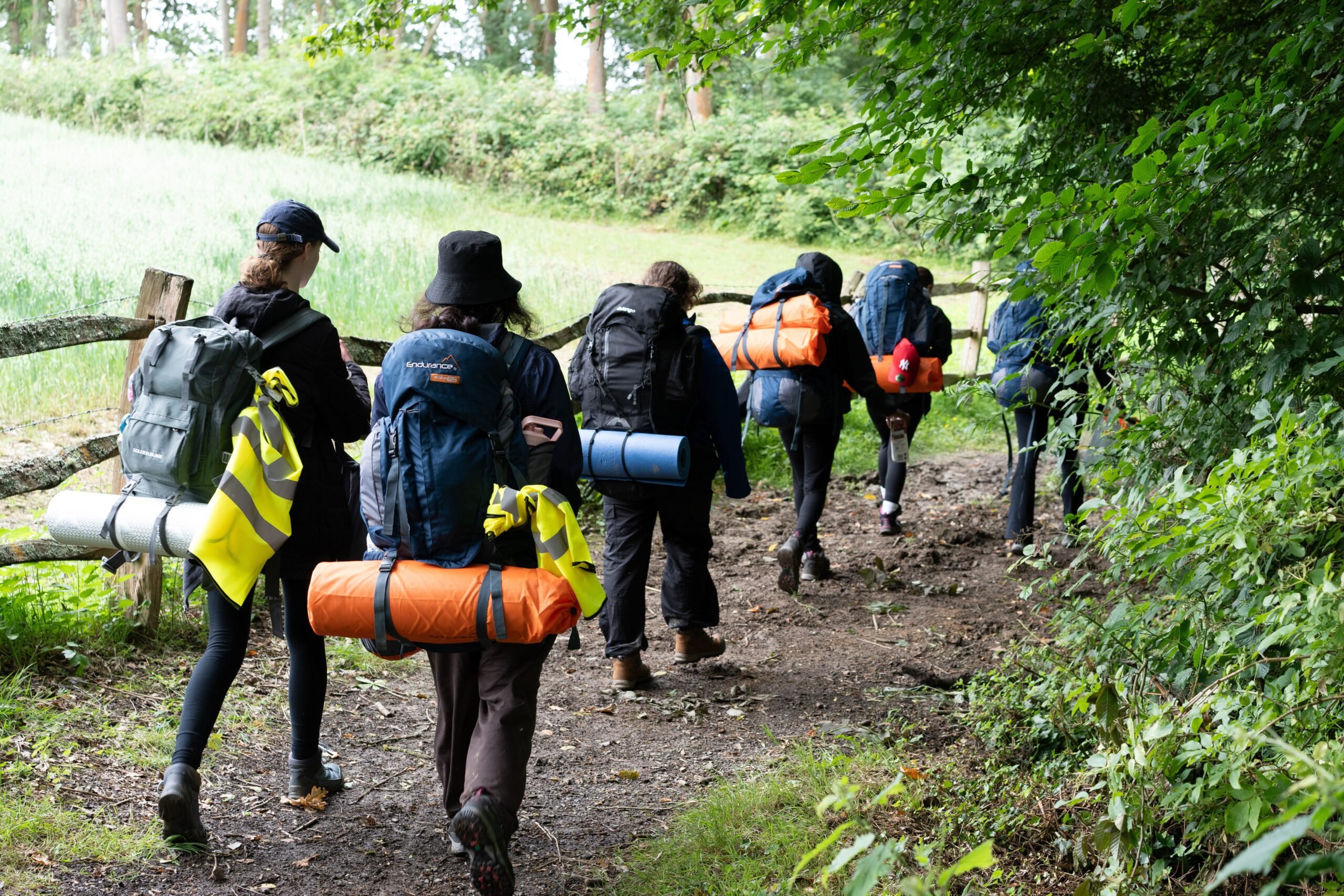 Six young people with full rucksacks walking along a woodland path.