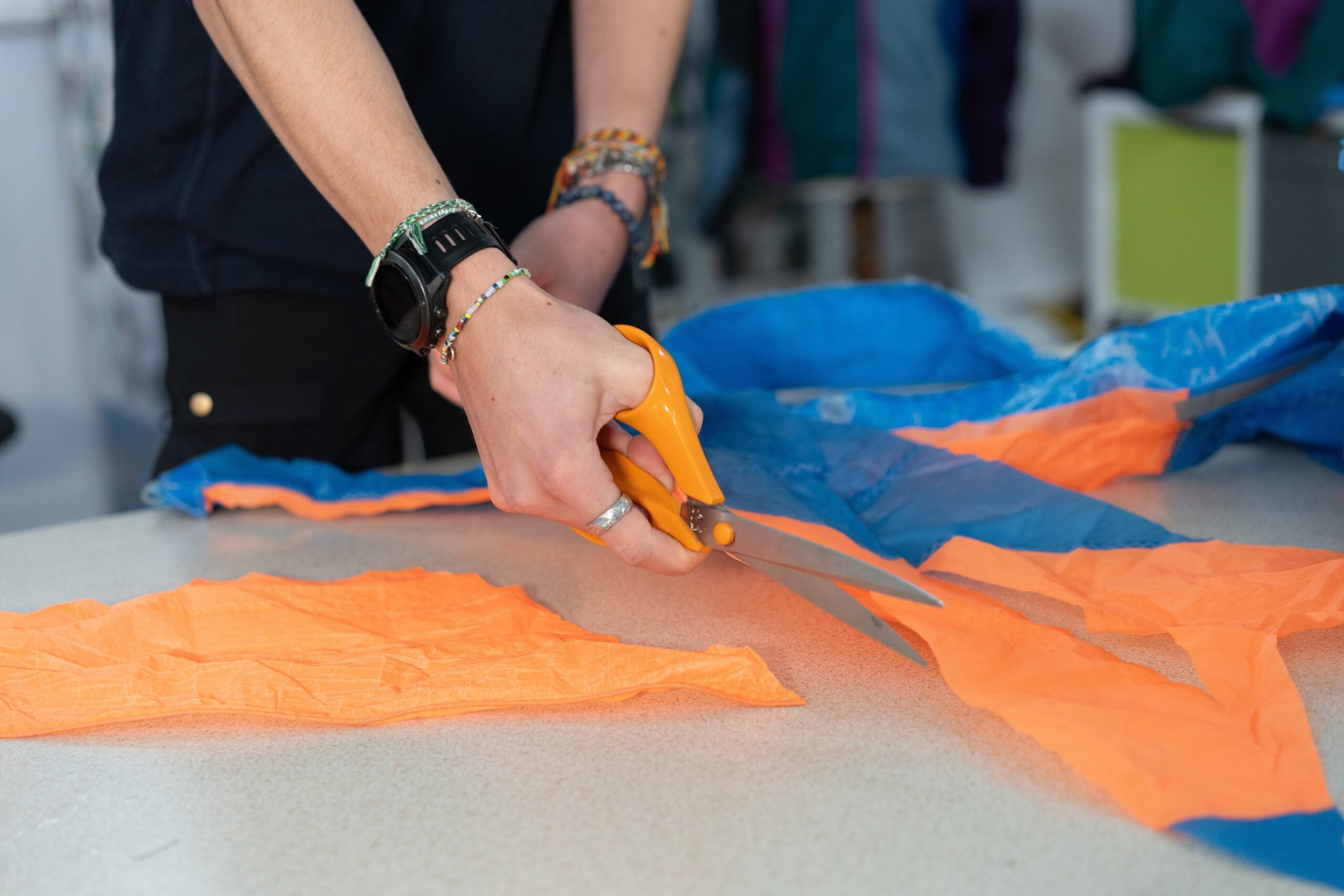 A pair of hands cutting orange and blue fabric with orange scissors.