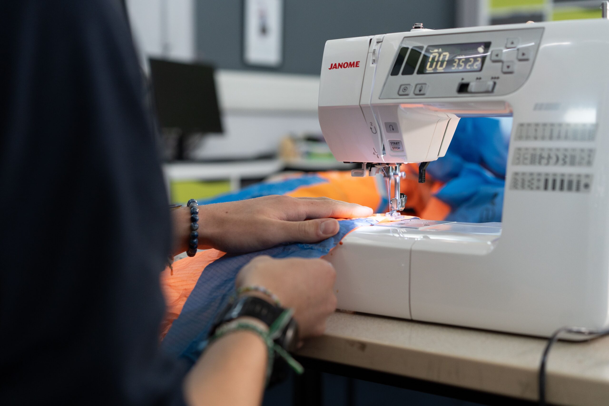 A young person sewing a blue and orange fabric on a sewing machine.
