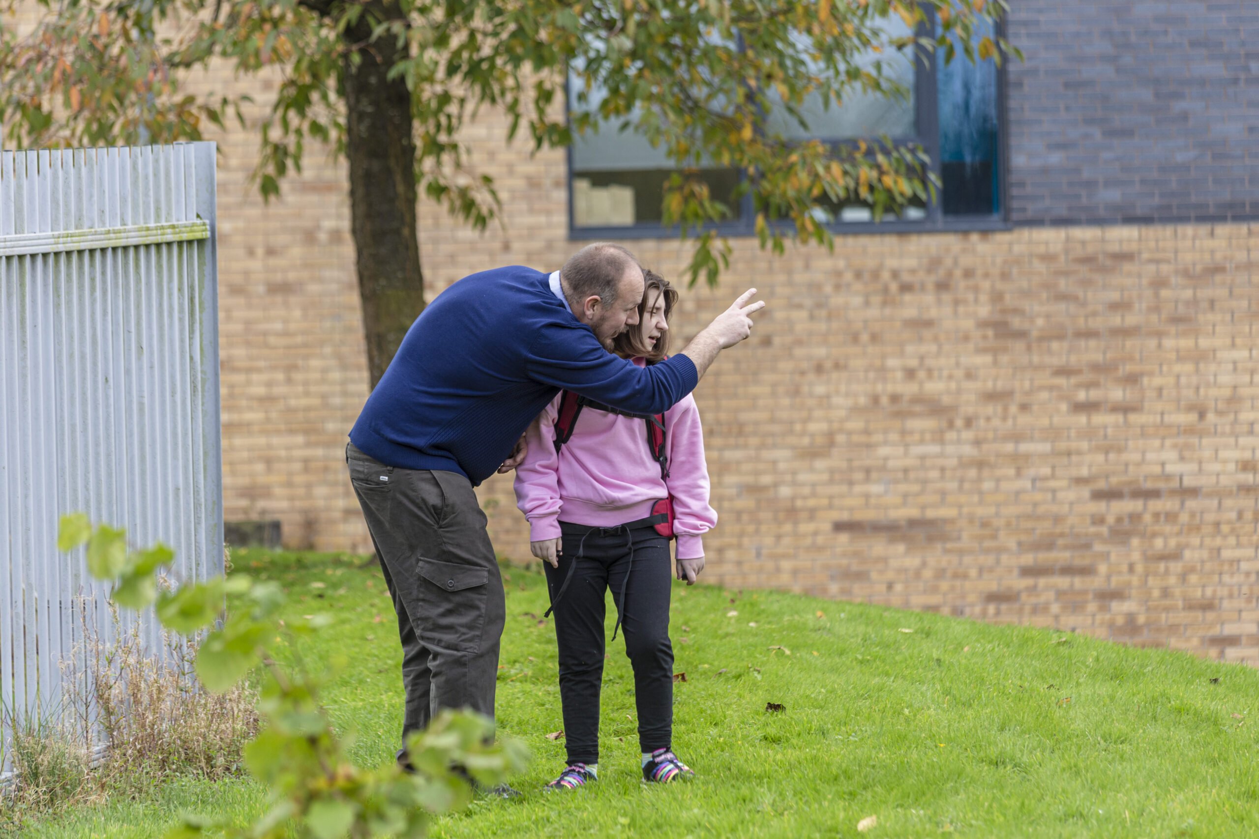 A D of E volunteer next to a young person pointing and looking to the right.