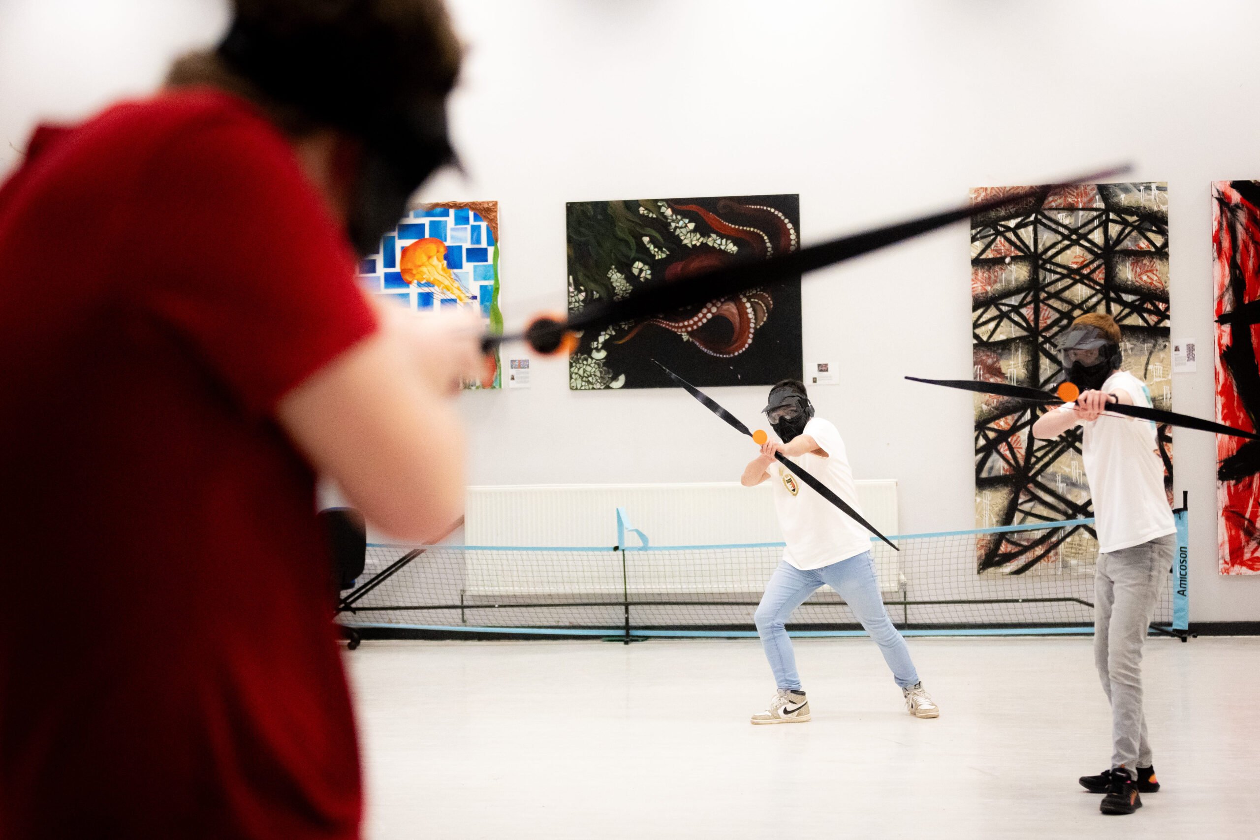 Three young people wearing safety masks play tag archery.