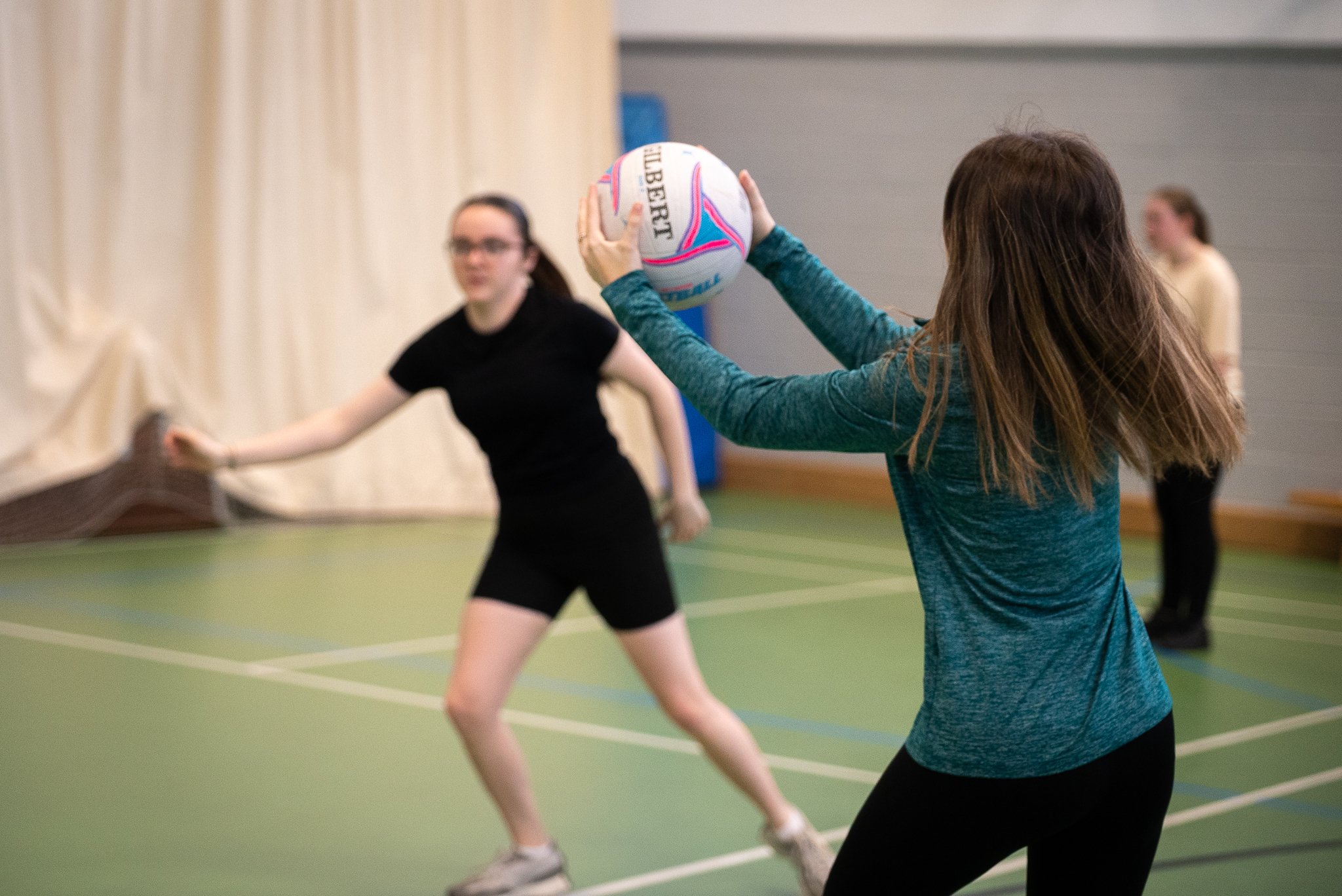 A young person catching a ball while playing sports with a group inside a hall.