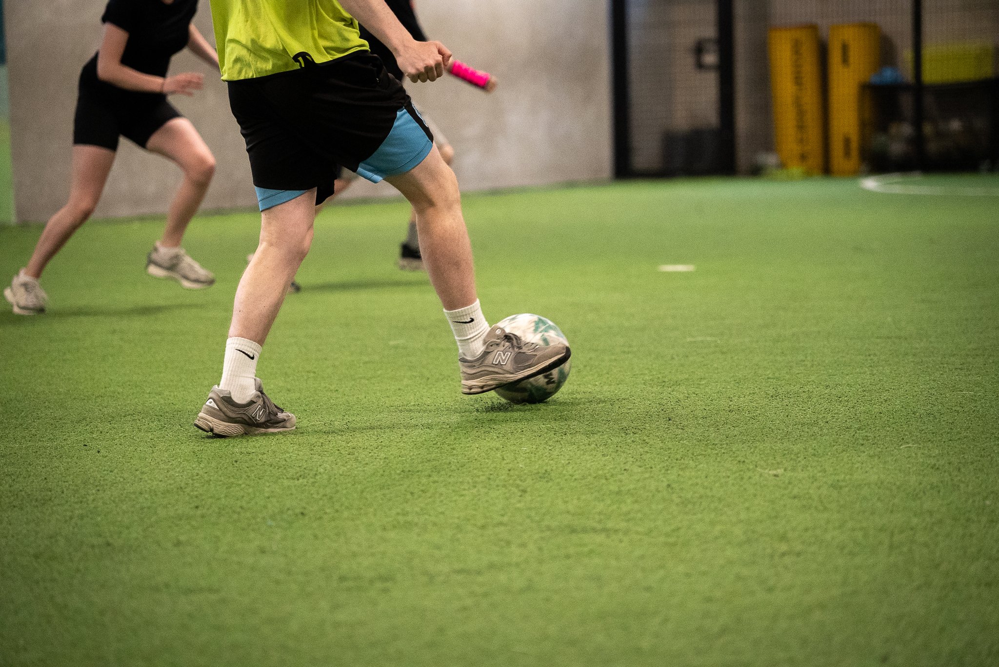 A pair of legs stopping a ball on an indoor football pitch.